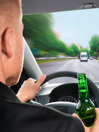 мужчина с бутылкой пива за рулем автомобиля в движении